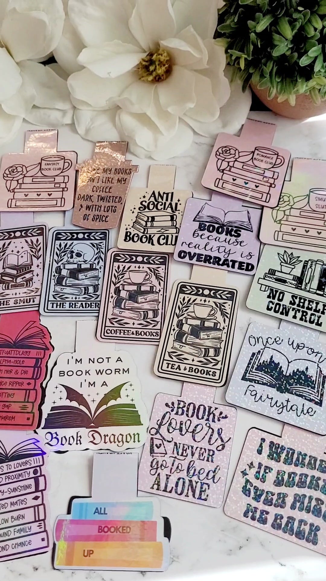 18 Magnetic bookmarks on a white marble background with foliage.