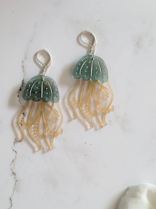 Close up of resin earrings in the shape of a blue and gold jelly fish with metallic accents.