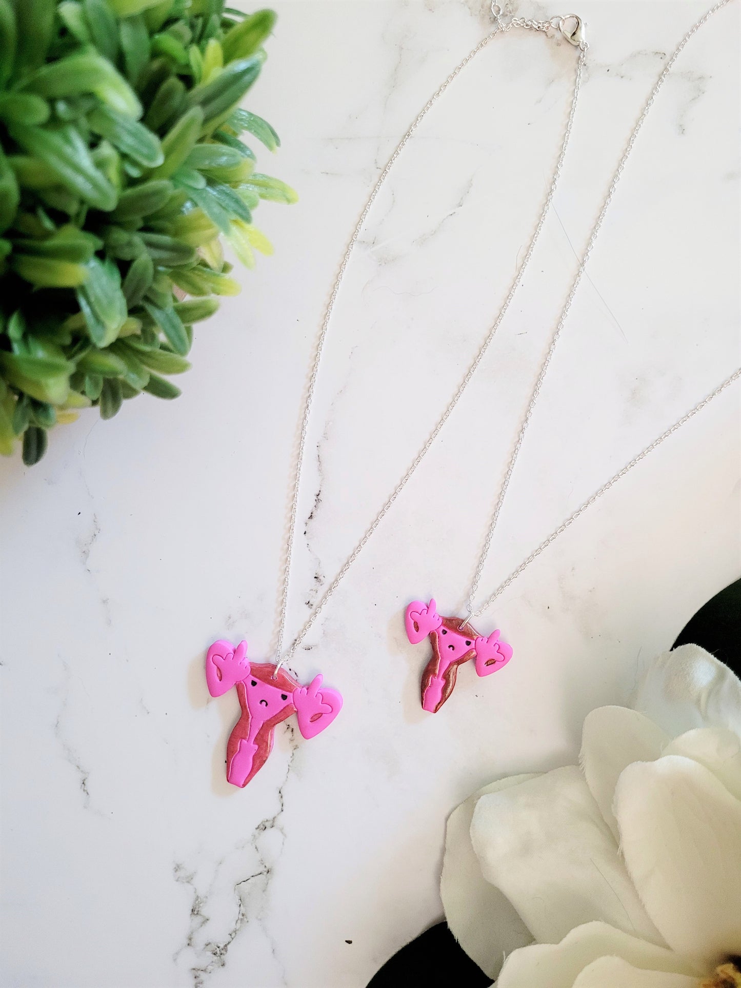 Pink uterus necklace with middle finger fallopian tubes.