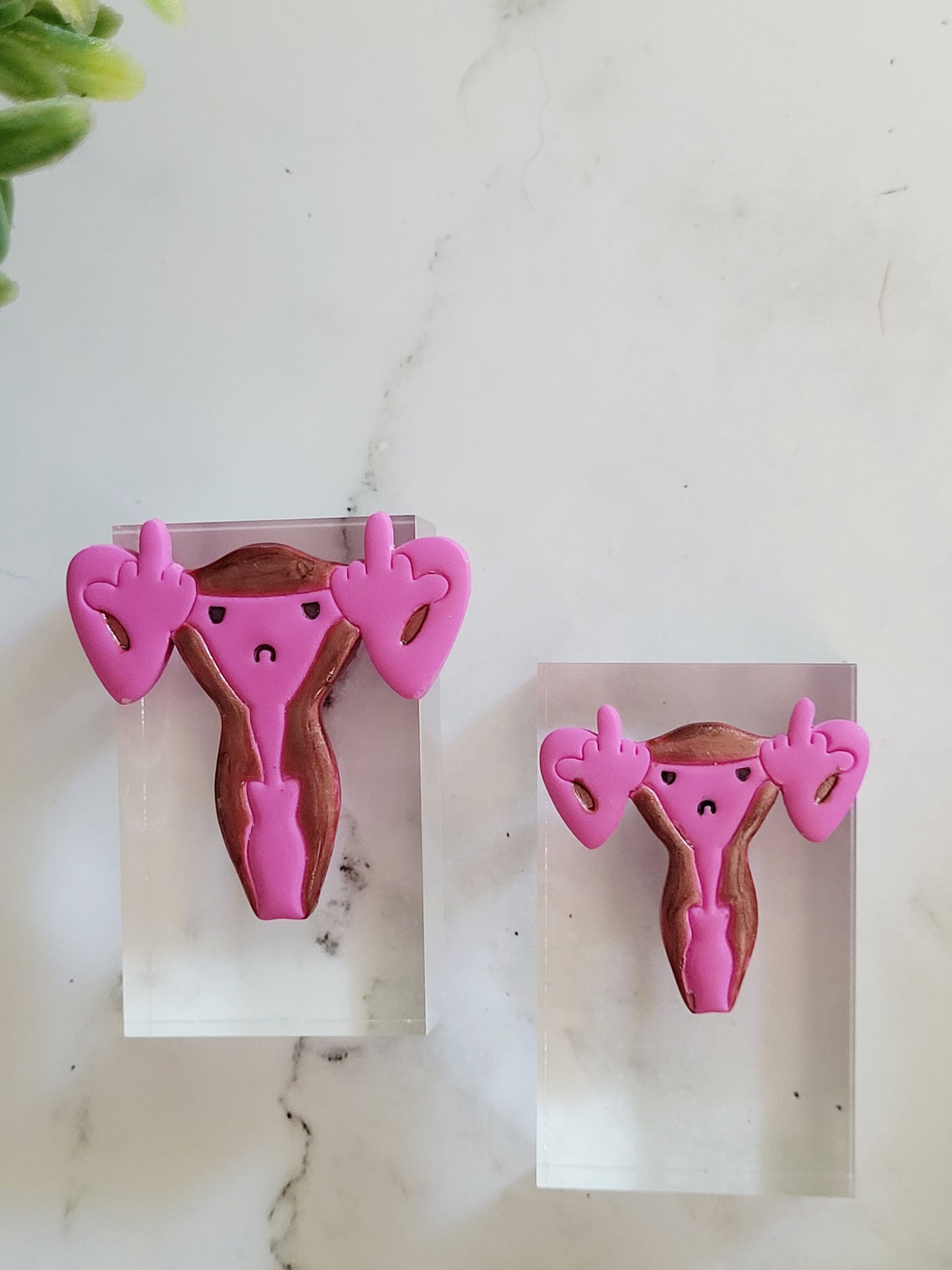 closeup of Pink uterus pin with middle finger fallopian tubes.