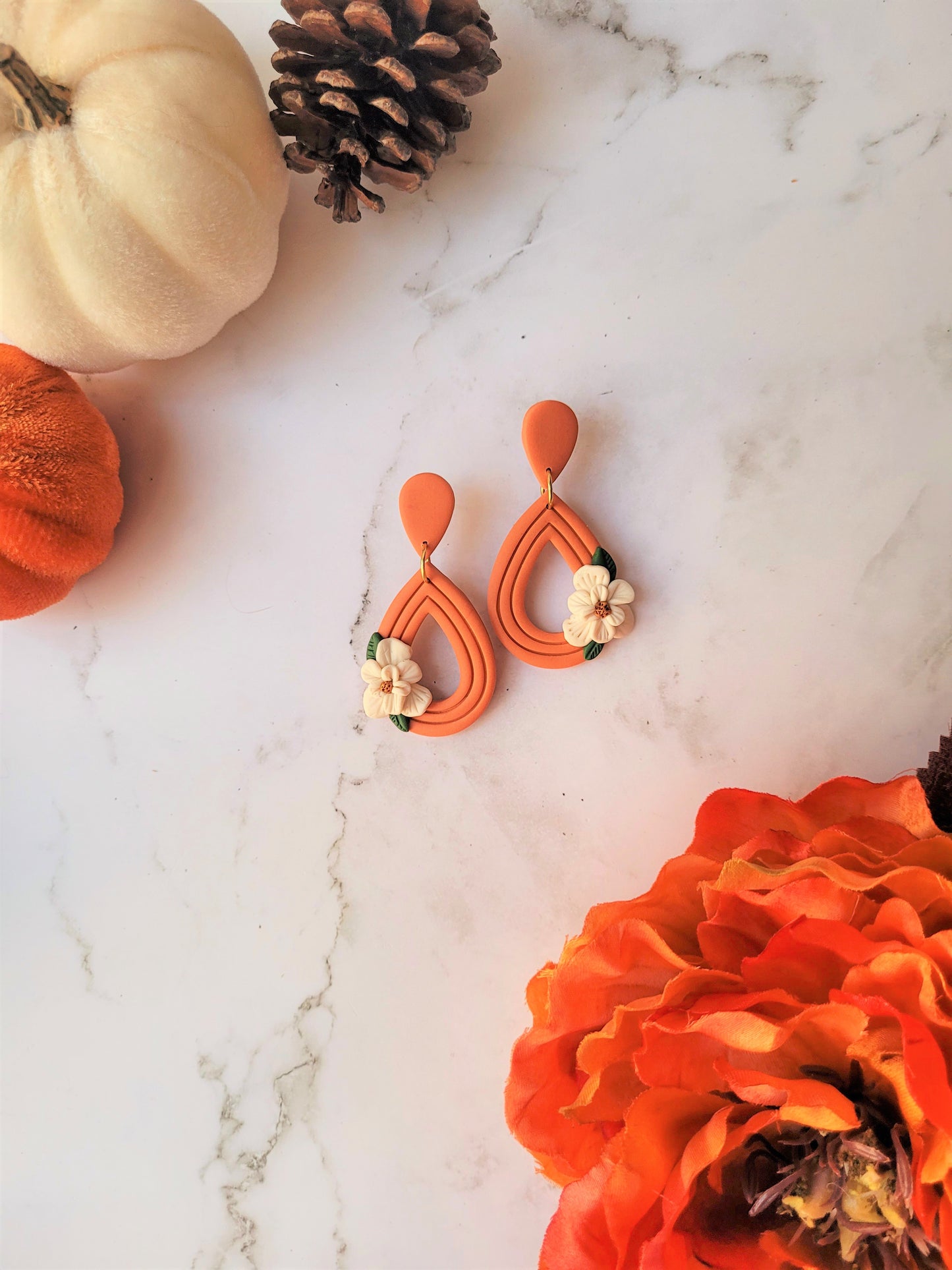 orange teardrop earrings with a white magnolia flower sitting on a marble background.