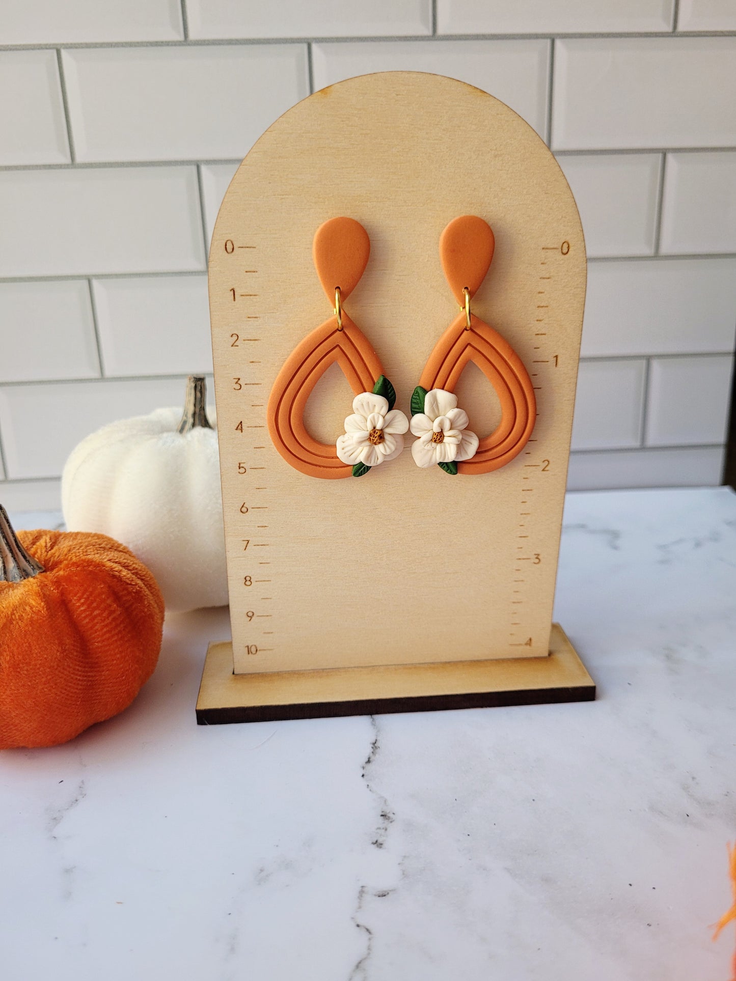 orange teardrop earrings with a white magnolia flower sitting on a ruler background.
