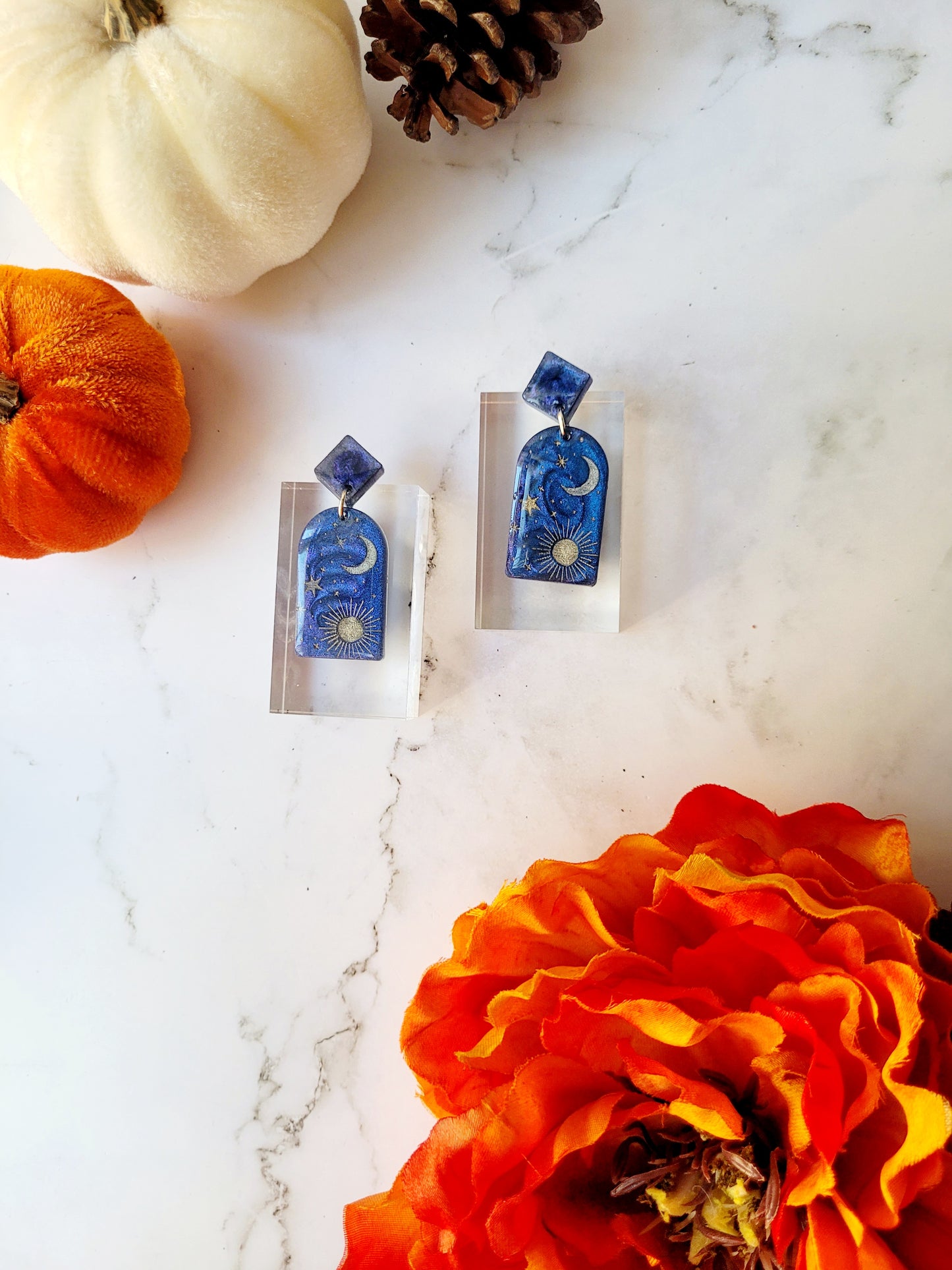 blue arch earrings with painted celestial details on a marble background.