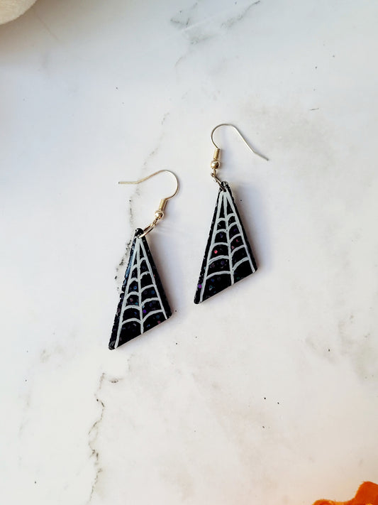 close up of asymmetrical black glitter earrings with white spider webs