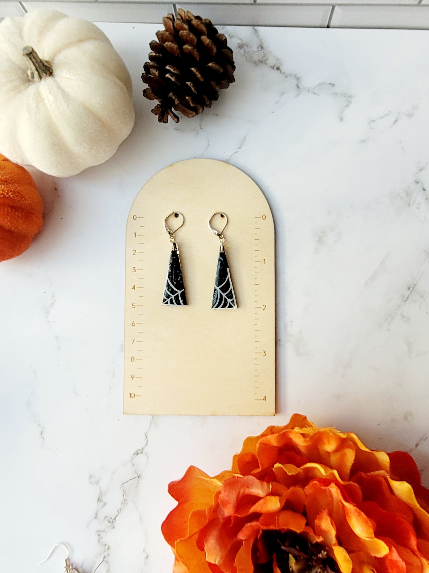 close up of triangular black glitter earrings with white spider webs on ruler
