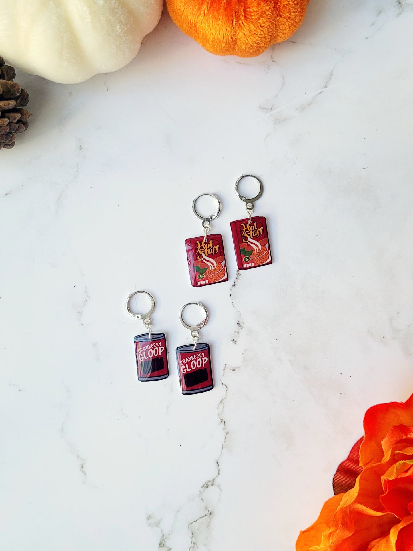 Cranberry sauce and stuffing box earrings on a marble background with fall foliage.