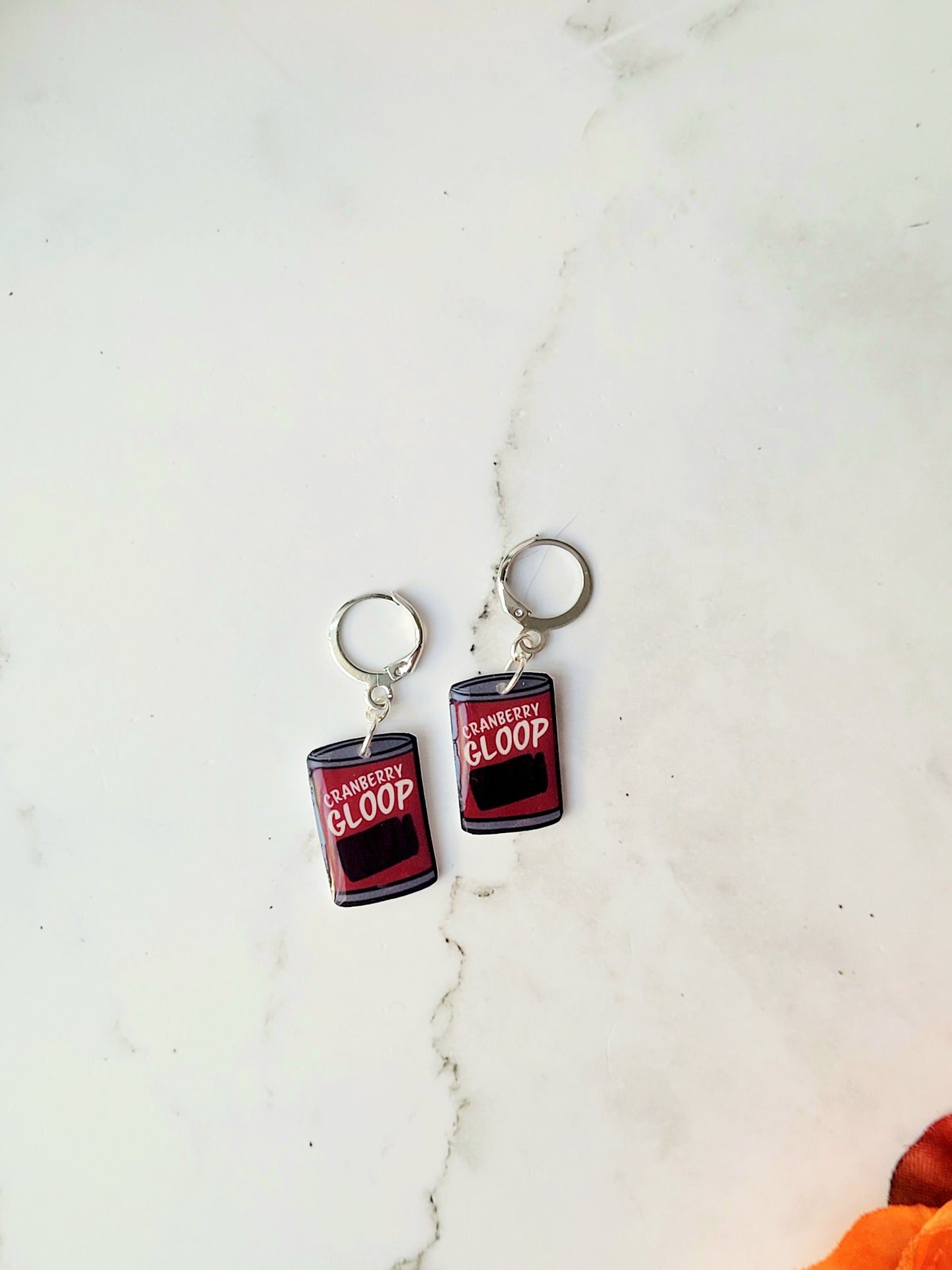 close up of Cranberry sauce earrings on a marble background with fall foliage.
