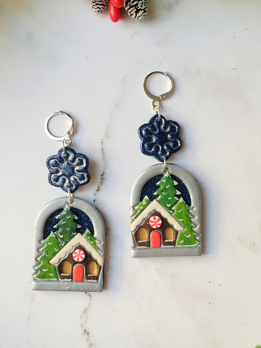 close up of painted winter landscape earrings on a marble background with foliage.