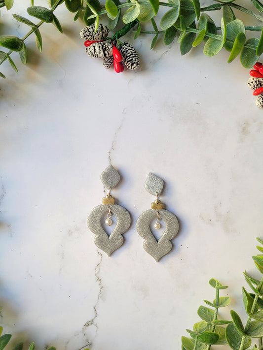 Silver glitter ornament shaped earrings with a pearl accent on a marble background with foliage.