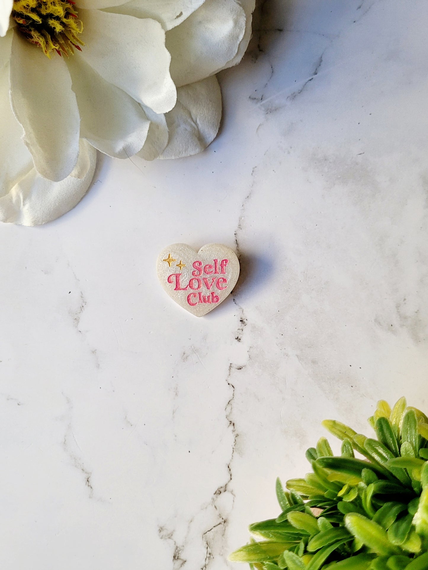 white pearl heart pin with self love club in pink on a marble background.
