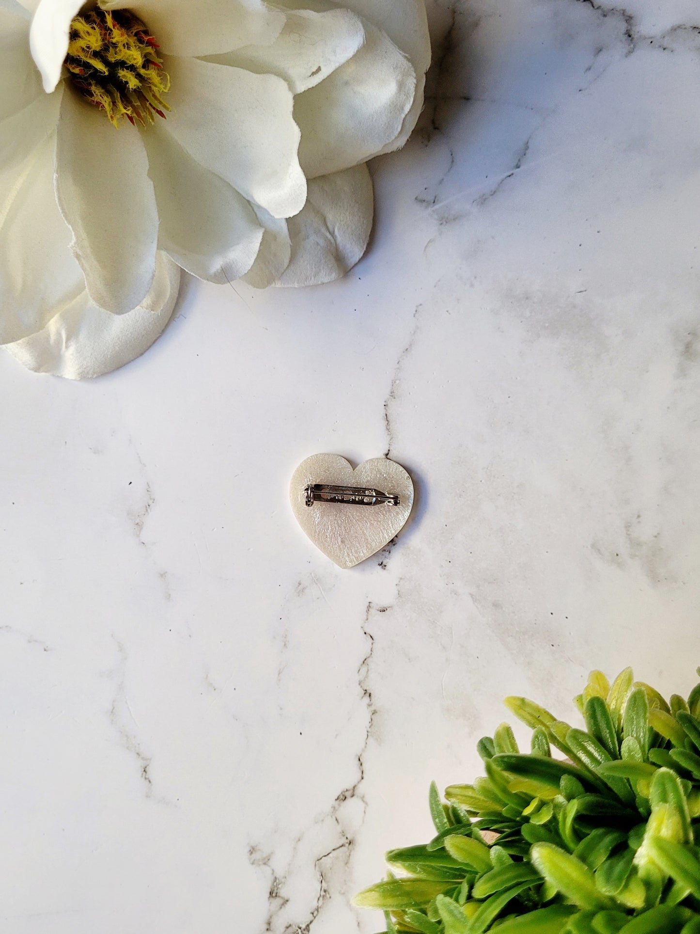 close up of the back of the white pearl heart pin on a marble background.