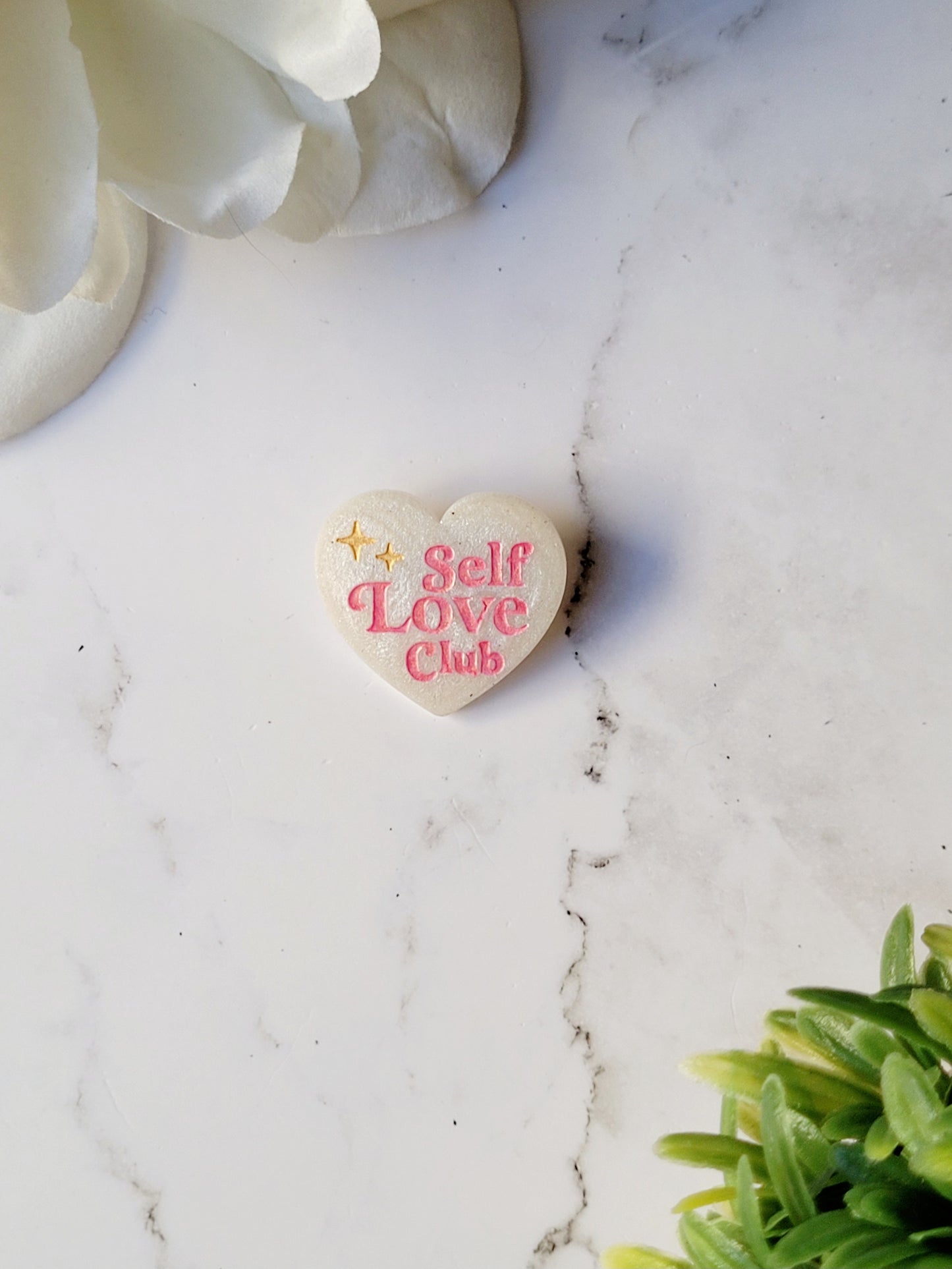 close up of white pearl heart pin with self love club in pink on a marble background.