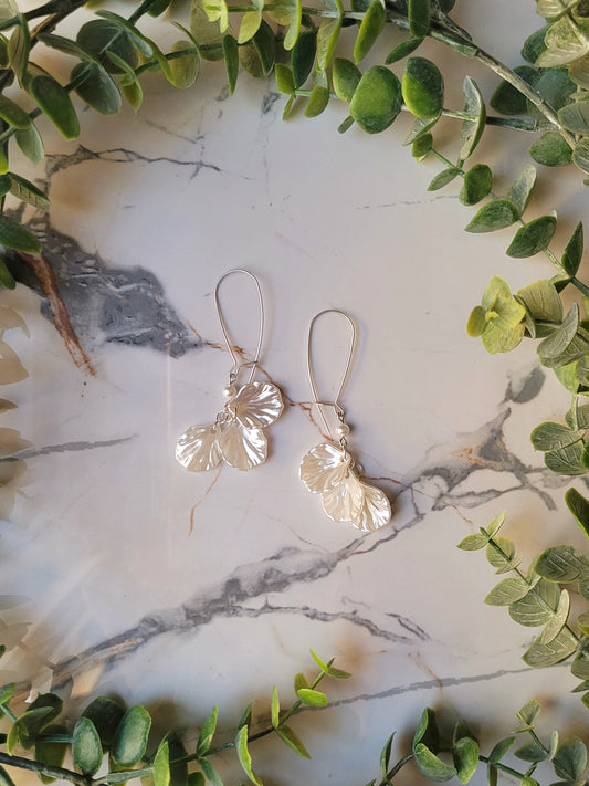 close up of pearl petal dangle earrings on a marble background and foliage.