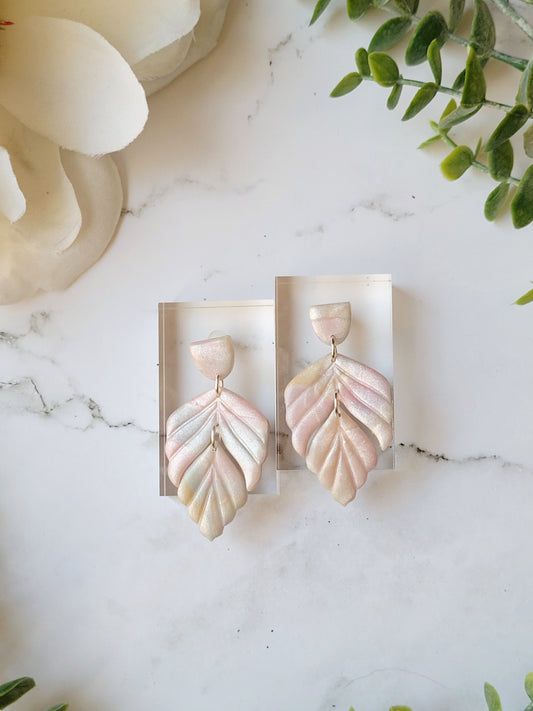 close up of faux mother of pearl clay earrings on a marble background surrounded by foliage.