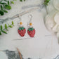 close up of Resin Strawberry and flower earrings with silver findings on a marble background surrounded by foliage.