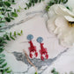Red Lobster with a blue shell stud earrings on a marble background with foliage. 