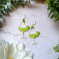 Lime margarita glass earrings on a marble background with foliage. 