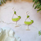 close up of Lime margarita glass earrings on a marble background with foliage. 