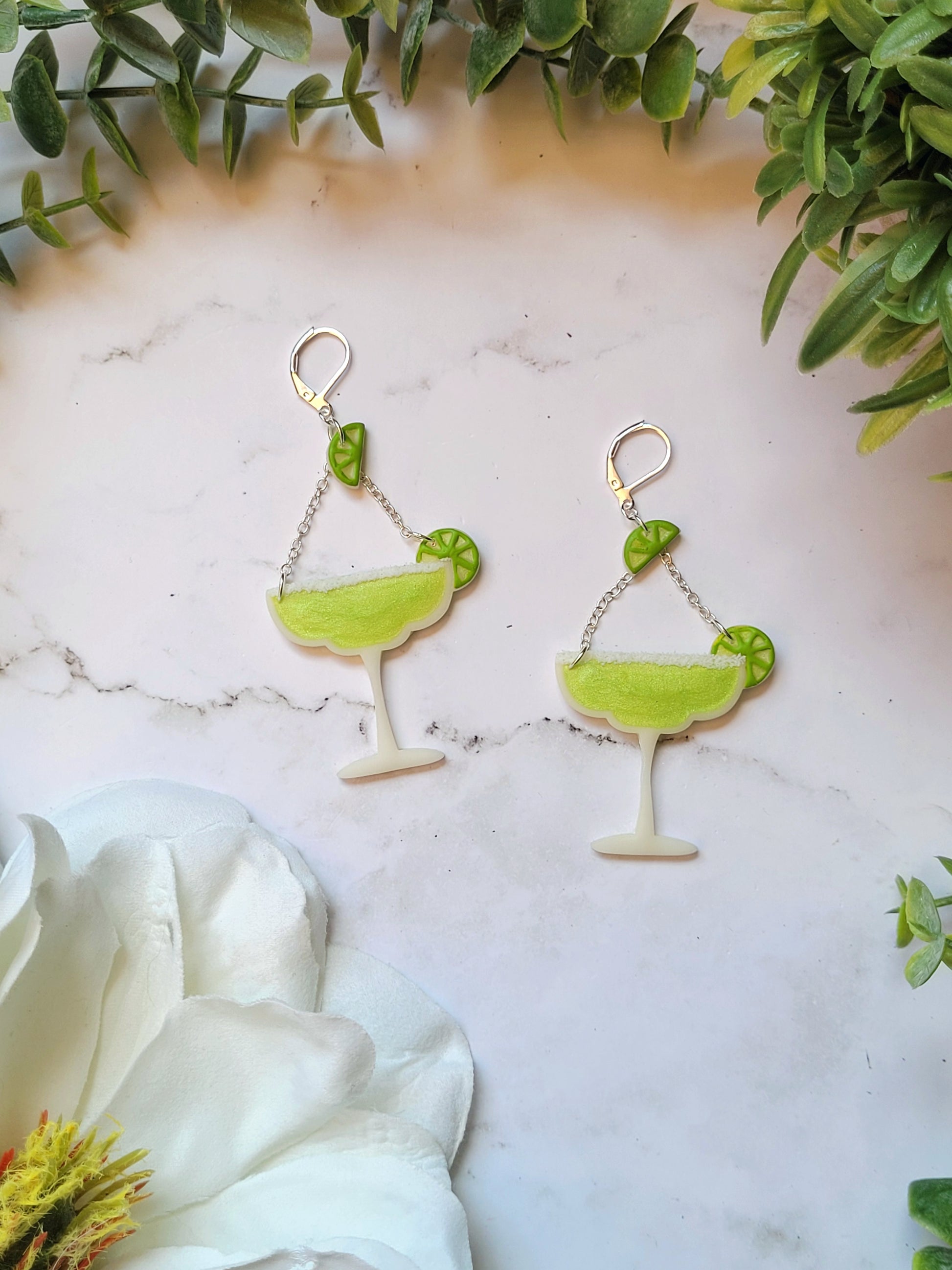 close up of Lime margarita glass earrings on a marble background with foliage. 