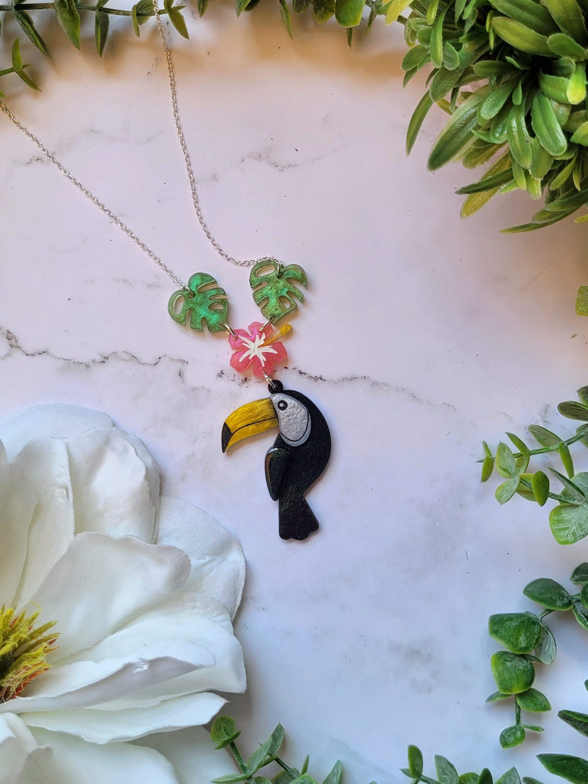 toucan necklace on a marble background with foliage. 