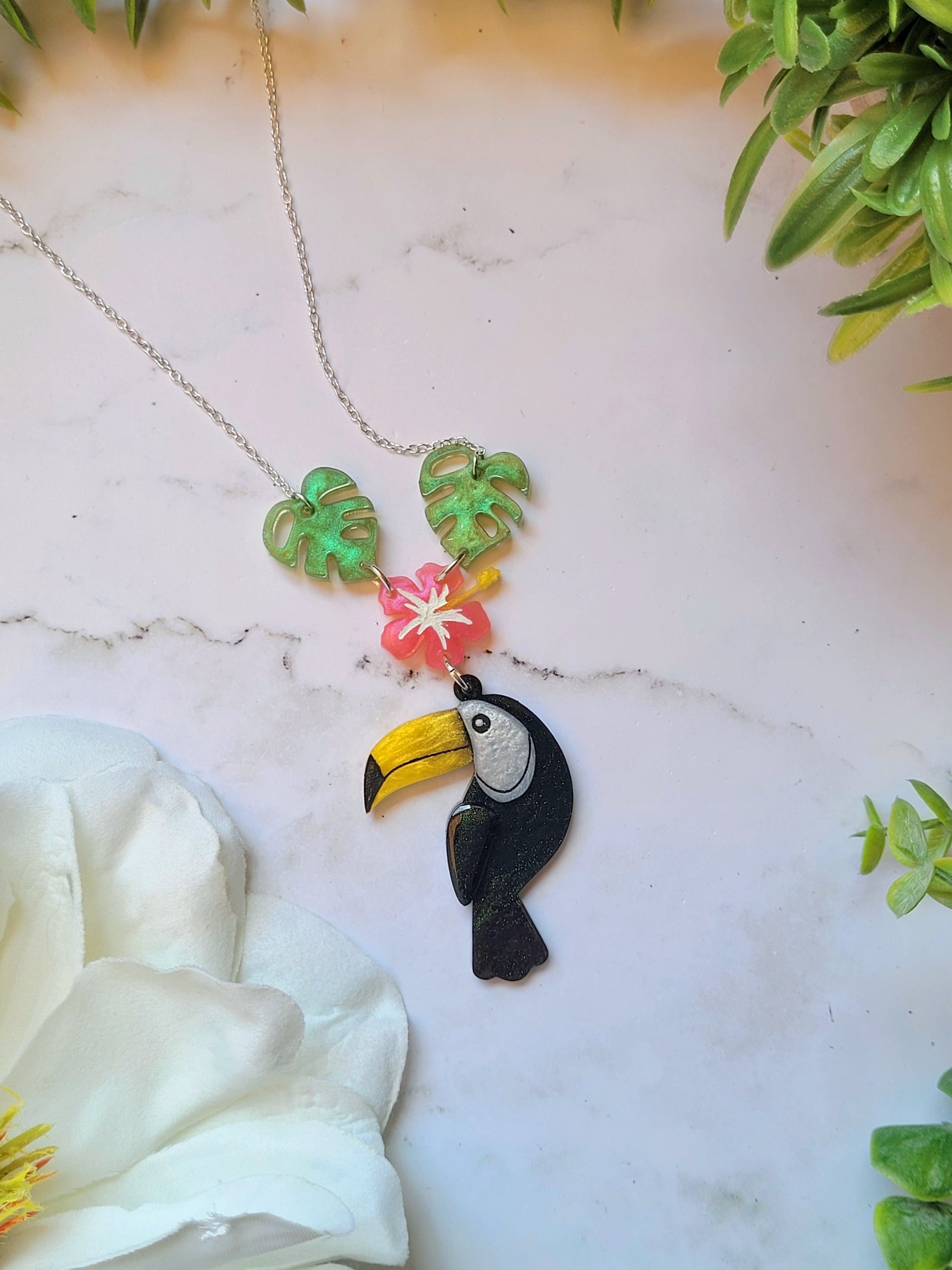 close up of toucan necklace on a marble background with foliage. 