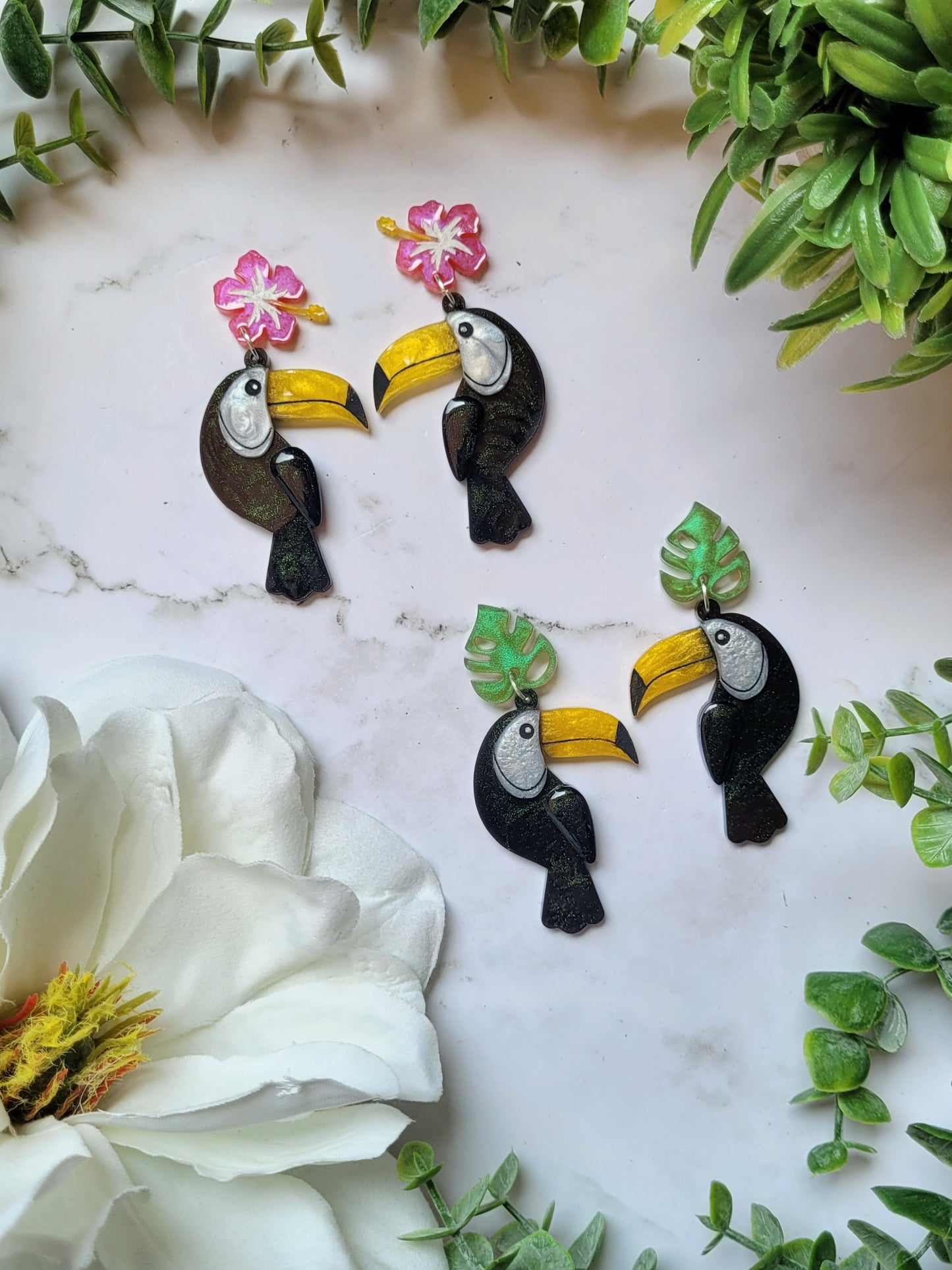 toucan earrings with flower and leaf charms on a marble background. 