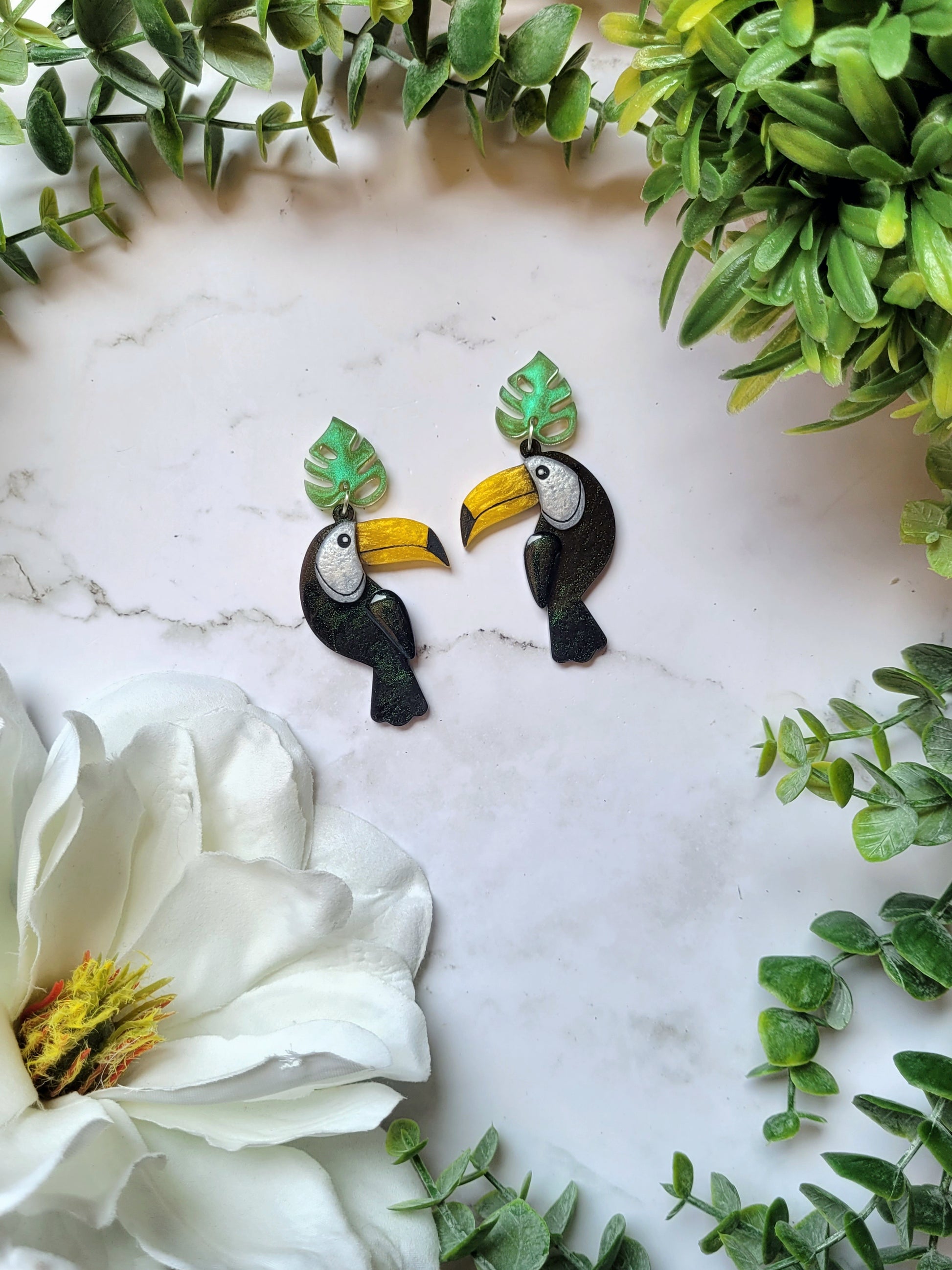 close up of toucan earrings with leaf charm on marble background. 