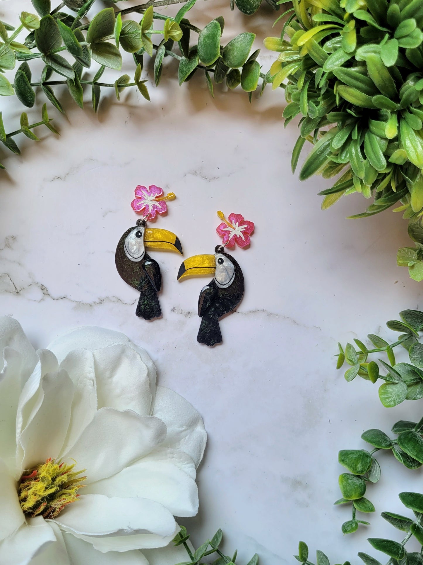 close up of toucan earrings with flower charm on marble background.