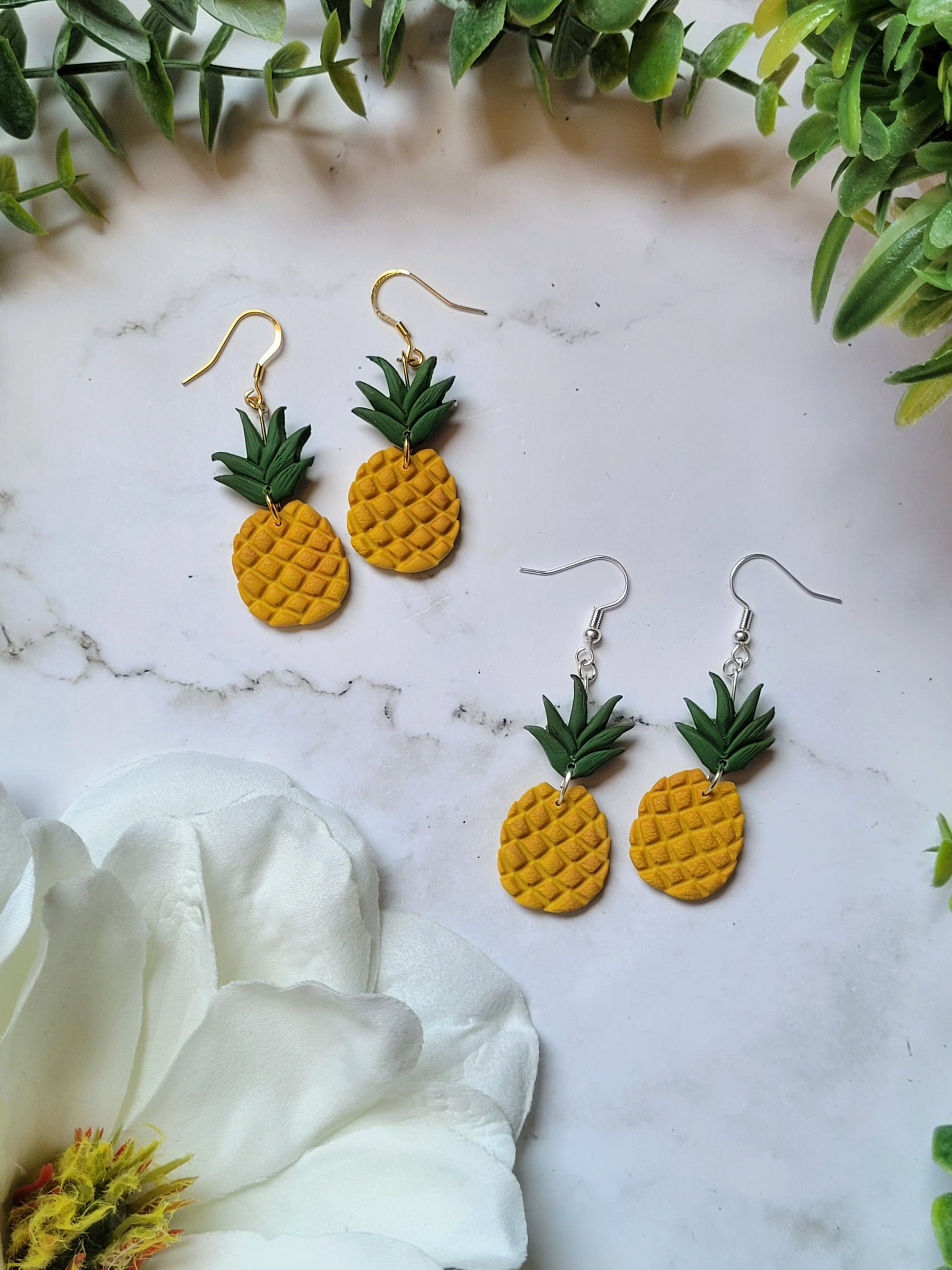 pineapple earrings on a marble background with foliage.