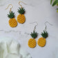 close up of pineapple earrings on a marble background with foliage.