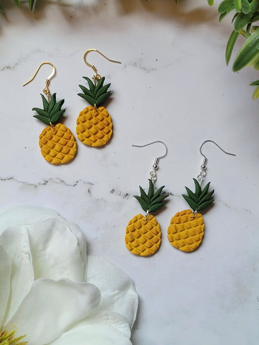 close up of pineapple earrings on a marble background with foliage.