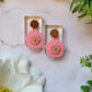 Baby pink flower earrings on white background with foliage. 