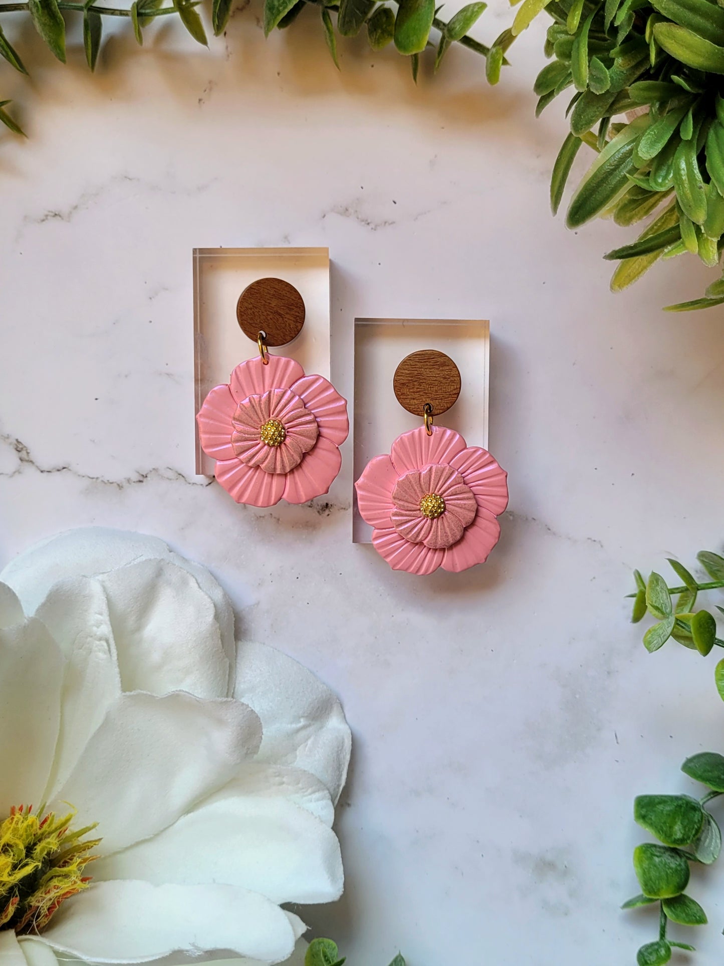 Baby pink flower earrings on white background with foliage. 