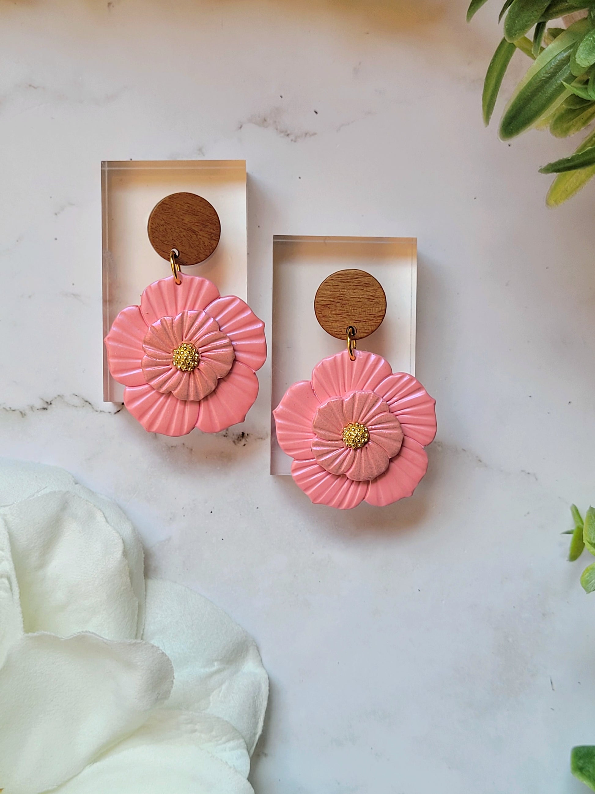 close up of Baby pink flower earrings on white background with foliage. 
