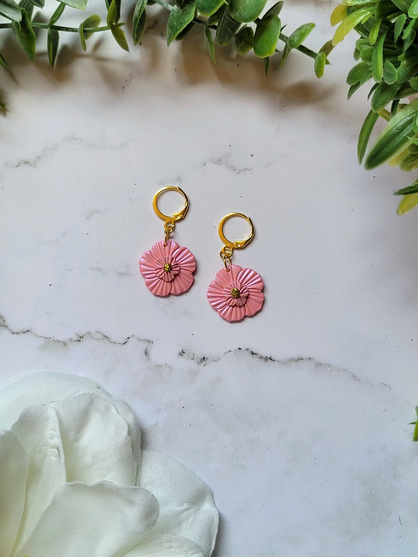 Baby pink flower earrings on white background with foliage. 