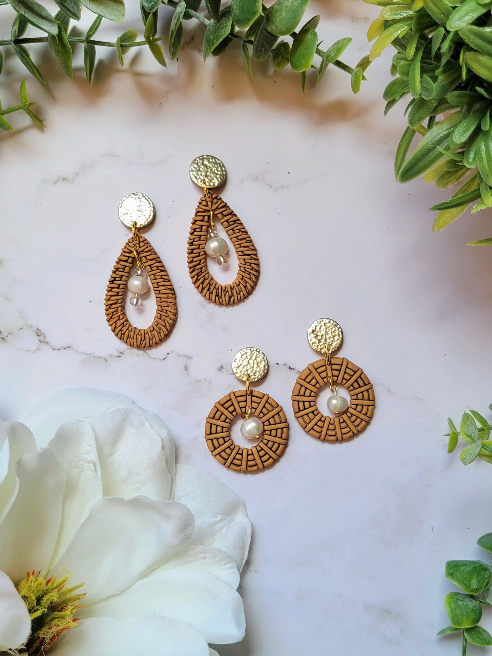 tear drop and round rattan earrings on a marble background with foliage. 