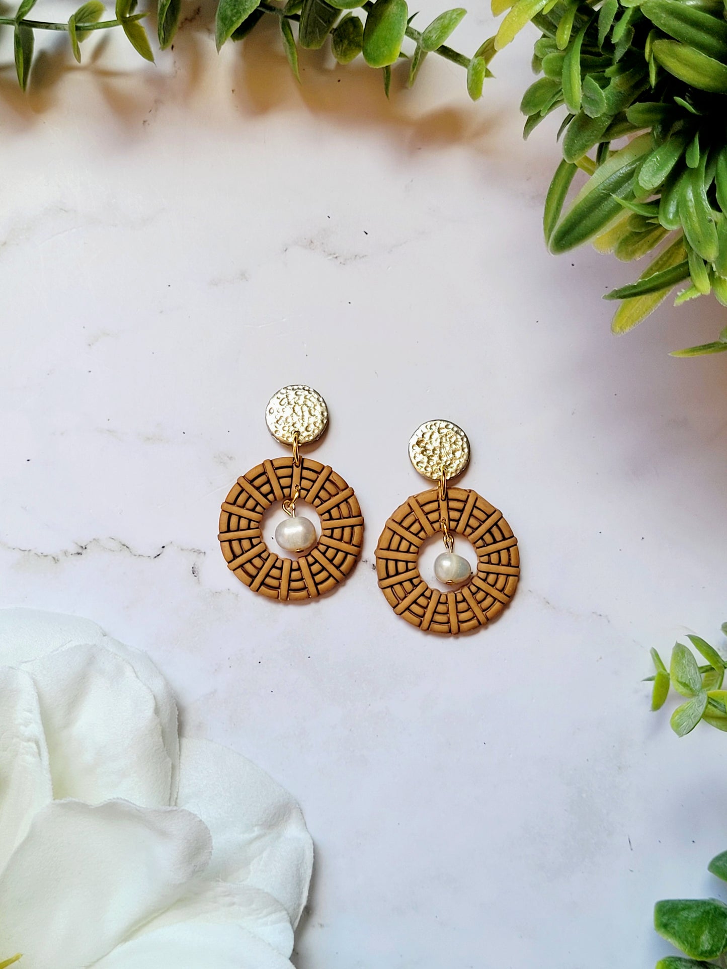 close up of round rattan earrings on a marble background with foliage.