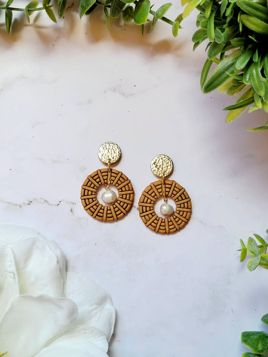 close up of round rattan earrings on a marble background with foliage.