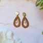 close up of tear drop rattan earrings on a marble background with foliage.