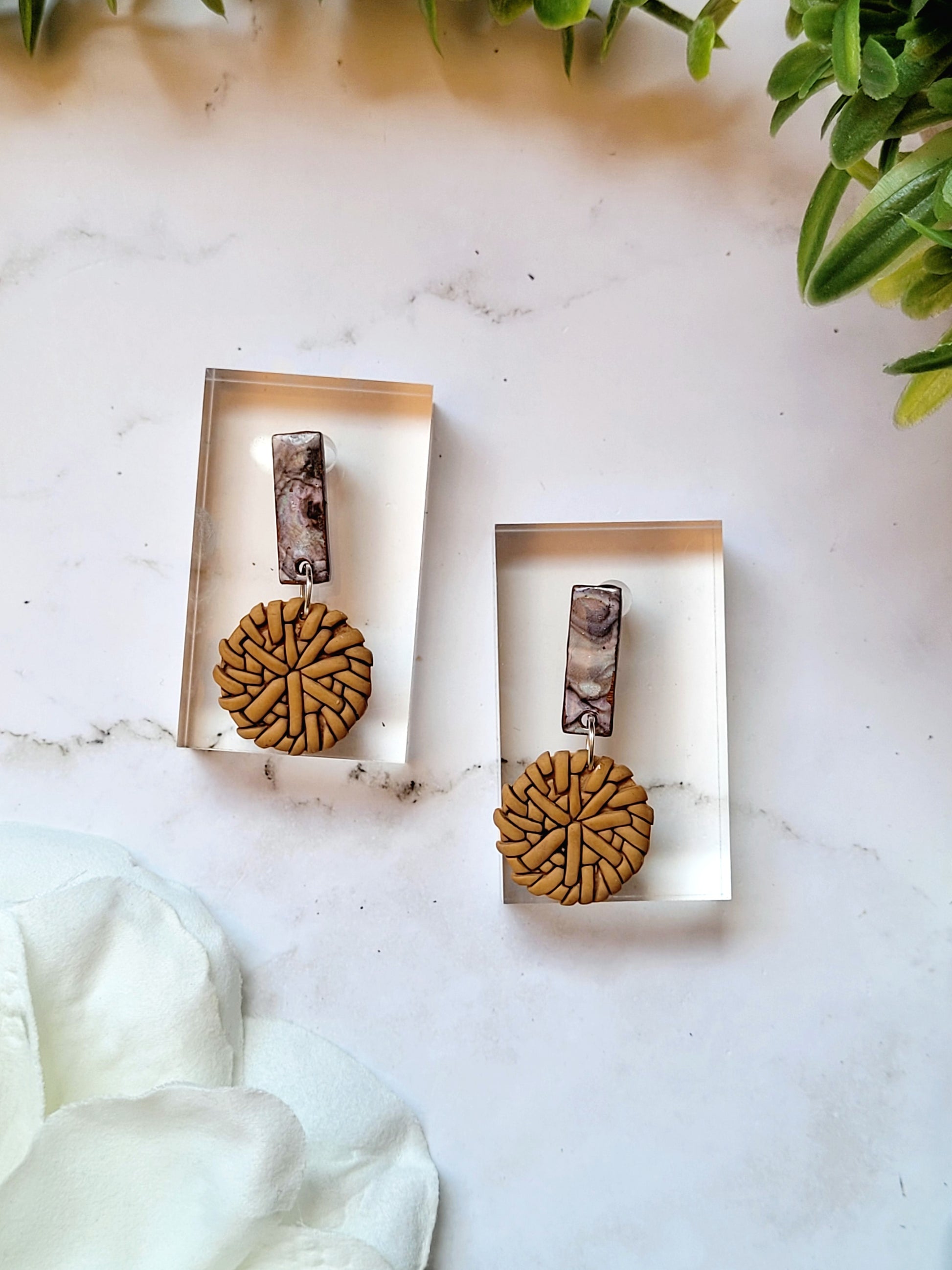 close up of Faux rattan and shell earrings on a marble background. 