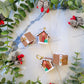 Gingerbread house earrings on a marble background surrounded by foliage. 