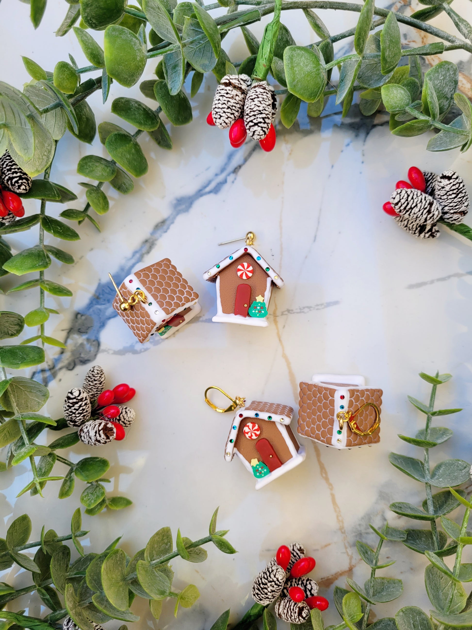 Gingerbread house earrings on a marble background surrounded by foliage. 
