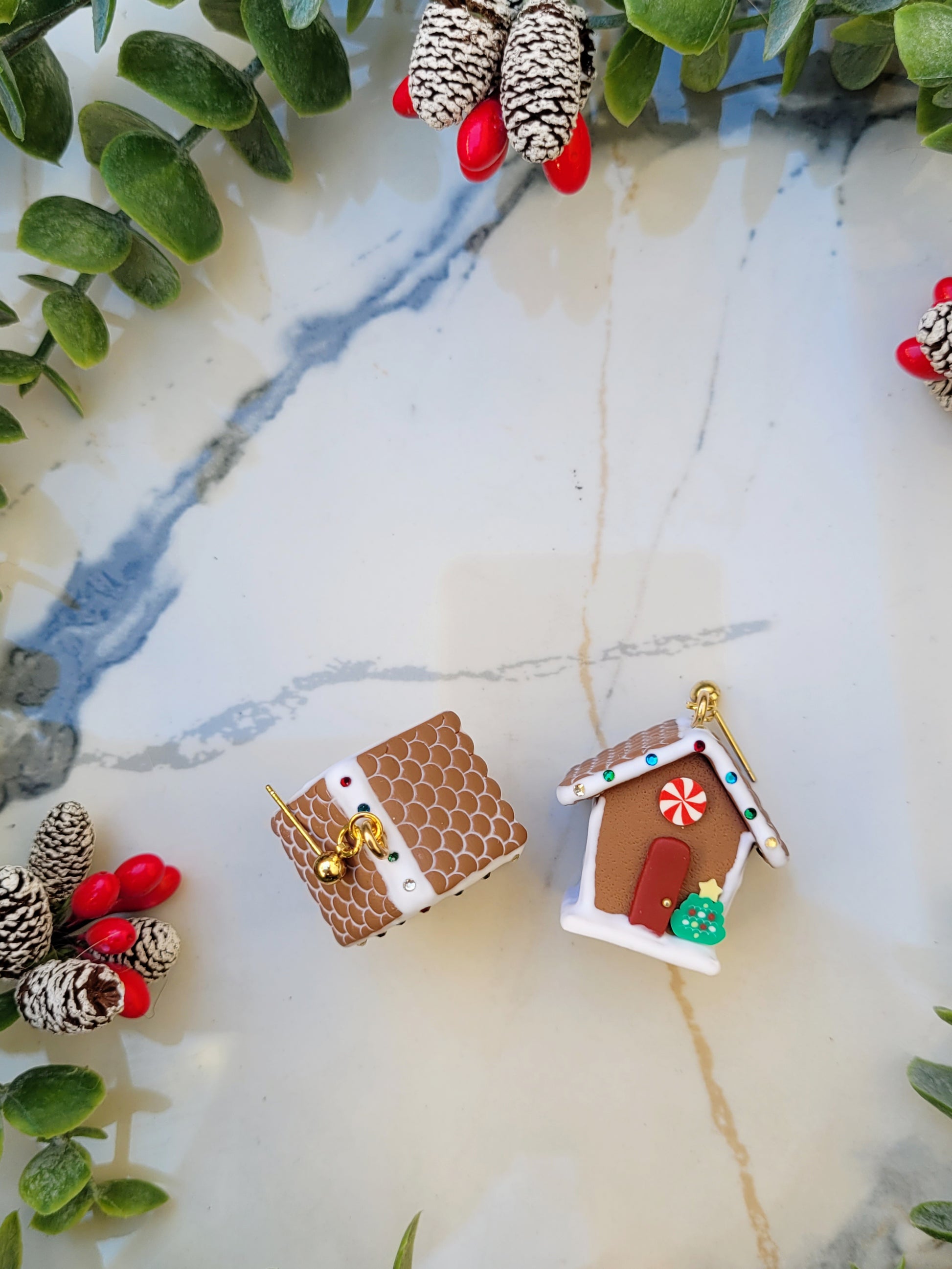 Close up of Gingerbread house earrings with stud back  on a marble background surrounded by foliage.