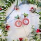 mistletoe and candy cane striped hoop earrings on a white marble background surrounded by foliage.