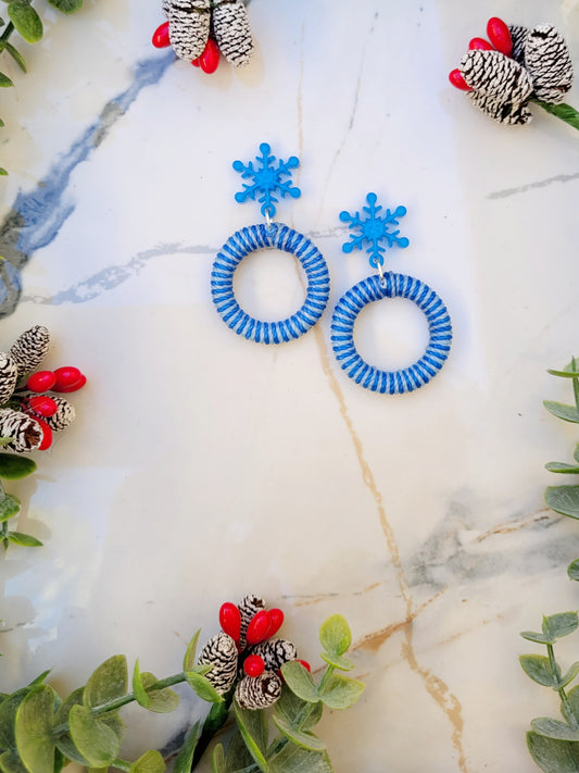 snowflake striped hoop earrings on a white marble background surrounded by foliage.