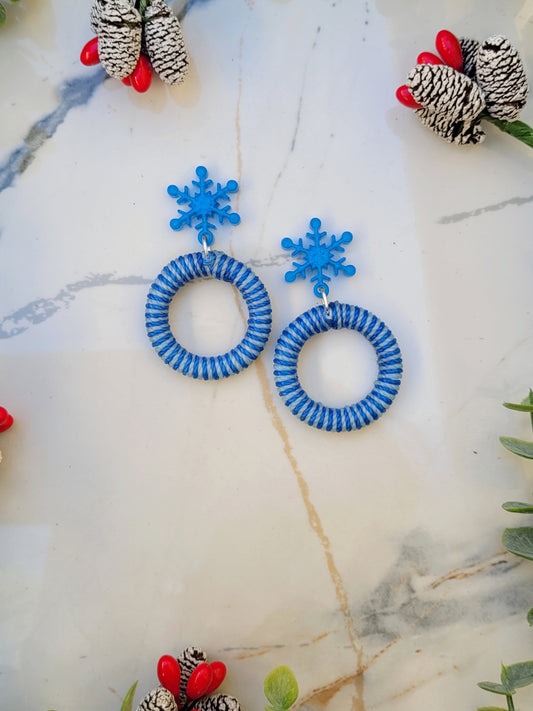  close up of snowflake striped hoop earrings on a white marble background surrounded by foliage.