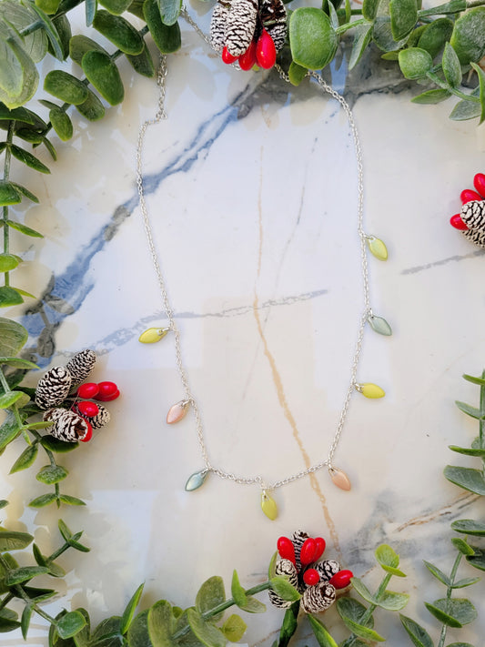 Christmas lights necklace on a marble background surrounded by foliage. 