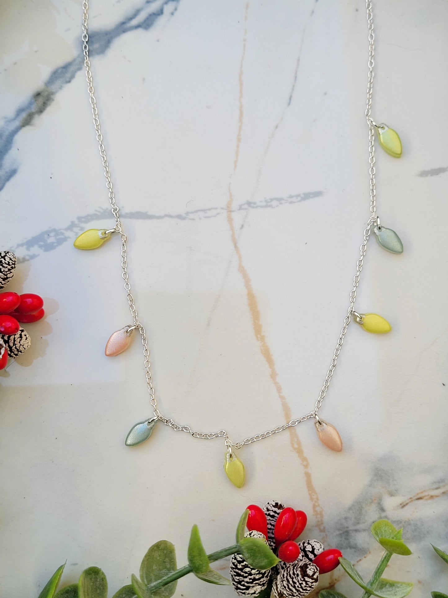 close up of Christmas lights necklace on a marble background surrounded by foliage.
