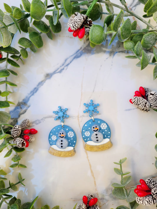 Snow globe earrings on a marble background with foliage. 