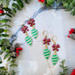 retro ornament style earrings on a marble background surrounded by foliage. 